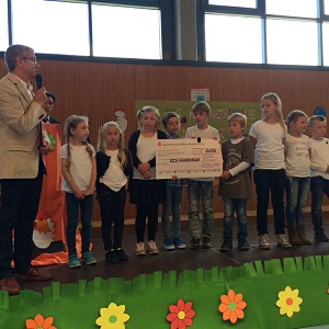 Rektor Gerd Brodde interviewt auf einer kleinen Bühne die Kinder der 4. Jarhgangsstufe, die soeben den Scheck in Höhe von 3050 Euro erhalten haben.