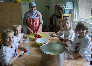 Vier Kinder der Villa Kunterbunt und die Erzieherin bereiten das Frühstück in der Küche vor. 